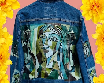 May include: A blue denim jacket with a painting of a woman's face on the back. The painting is in a cubist style and features geometric shapes and colors.