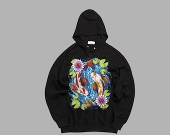 May include: Black hoodie featuring a colorful illustration of two koi fish swimming in a pond with water lilies. The koi are orange and white, set against a blue background. The hoodie has a drawstring hood.