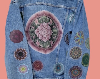 May include: A blue denim jacket with a large floral mandala painted on the back and smaller mandalas painted on the sleeves. The mandalas are in shades of pink, green, purple, and blue.