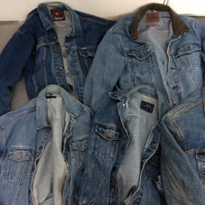 May include: Four denim jackets in various shades of blue, some with corduroy collars. The jackets are laid out on a white surface, with the collars and pockets visible.