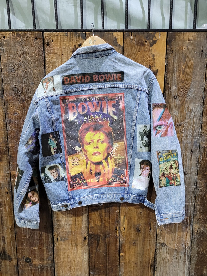 May include: A blue denim jacket with various David Bowie patches and images, including a poster for his "Ziggy Stardust" tour at Carnegie Hall.