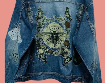 May include: A blue denim jacket with a large green moth and floral design on the back. The design includes the text "MOTTEO MY MUSE" and several smaller butterflies.