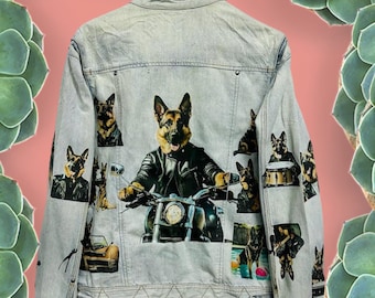 May include: Light blue denim jacket featuring multiple images of a German Shepherd dog in various poses, including one riding a motorcycle. The jacket has a classic collar, button closure, and pockets. The dog images are in a cartoon style.