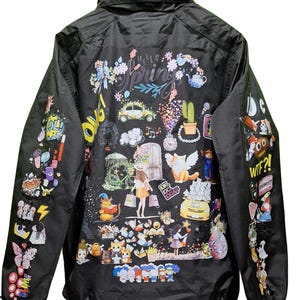 May include: Black nylon jacket with colorful graphic illustrations. The back features the words "Hello Spring" surrounded by flowers and whimsical images. Sleeves are decorated with various cartoon-style images. A collared jacket with a zipper closure.