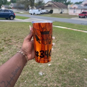 May include: A brown and gold stainless steel tumbler with a wood grain design. The tumbler features a black and white image of the coat of arms of the United States Virgin Islands and the number "#340" printed on the side.