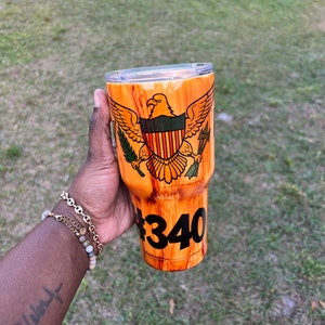 May include: A brown and orange wood-grain tumbler with a US Virgin Islands flag design and the number "#340" printed on the side.