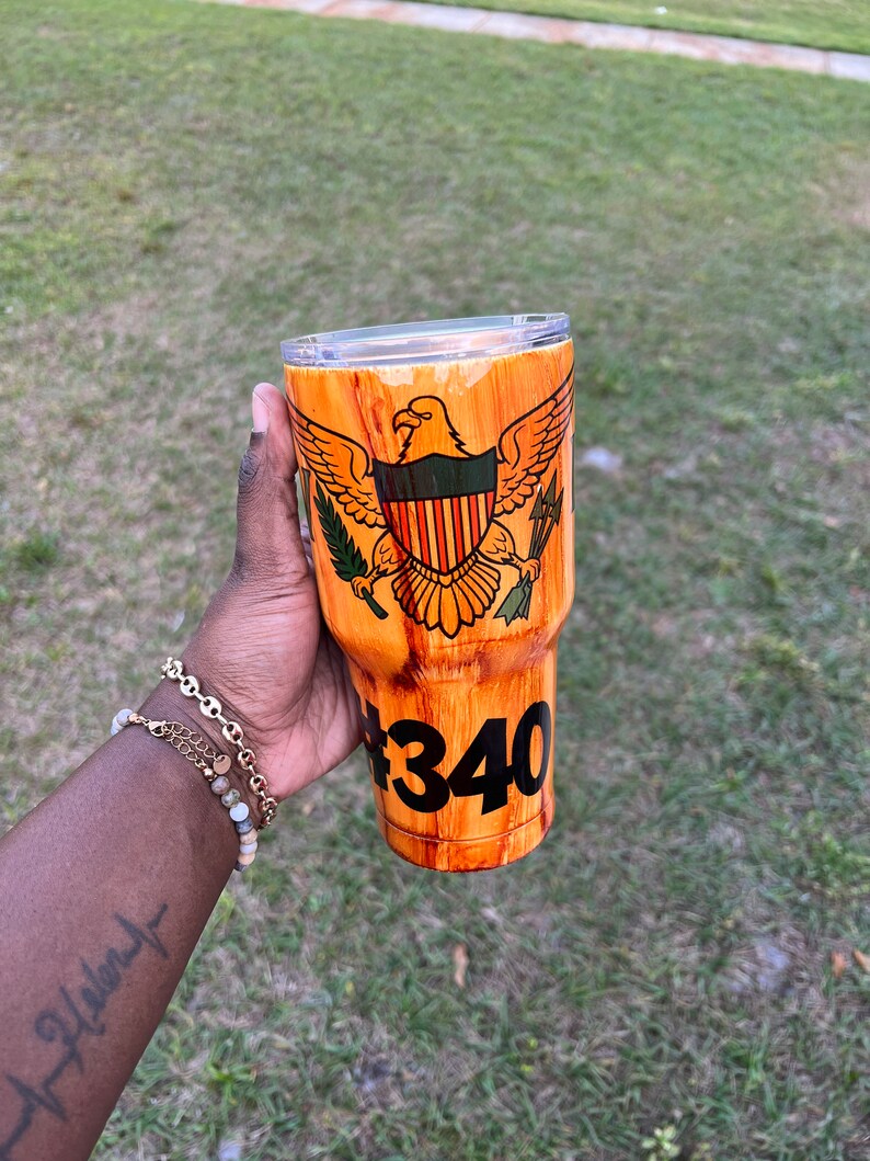 May include: A brown and orange wood-grain tumbler with a US Virgin Islands flag design and the number "#340" printed on the side.