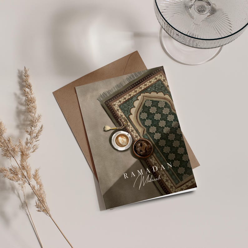 May include: A greeting card with a brown background and a green and brown patterned prayer rug. The card has the text "Ramadan Mubarak" in white lettering.