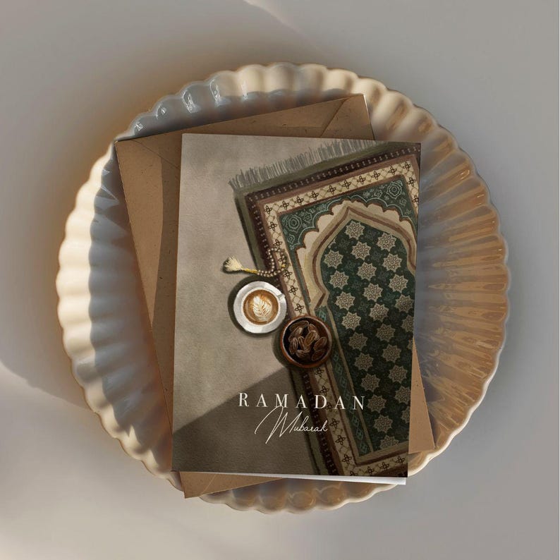 May include: A greeting card with a green and brown patterned prayer rug, a cup of coffee, and dates. The card says "Ramadan Mubarak".