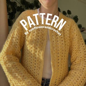 以下が含まれることがあります： レース模様とベルスリーブのついた黄色のクロシェカーディガン。カーディガンはボタン留めになっており、人が着用しています。画像には「PATTERN By sunflowerandcrochet」というテキストが重ねられています。