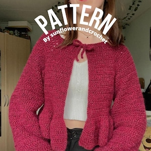 May include: A pink crocheted cardigan with a tie at the neckline. The cardigan has a ruffled hem and long sleeves. The text "PATTERN BY sunflowerandcrochet" is visible on the image.
