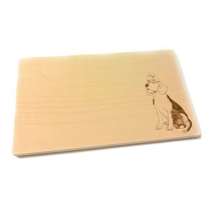 Könnte beinhalten: Rechteckiges Schneidebrett aus hellem Holz. Auf der rechten Seite befindet sich eine gravierte Illustration eines Hundes mit einem Hasen auf dem Kopf. Der Hund ist schwarz und weiß.