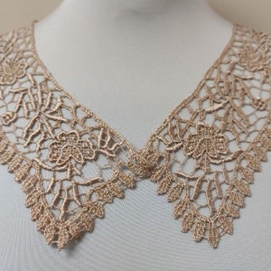 Puede incluir: Un delicado cuello de encaje beige con un patrón floral. El cuello está hecho de un encaje fino e intrincado y tiene un borde festoneado.