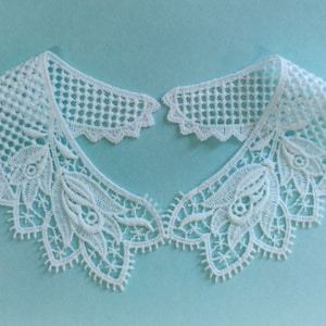May include: White lace collar with a delicate floral pattern. The collar is made of a fine, lightweight fabric and has a scalloped edge.