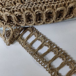 Op de afbeelding: Een close-up van een bruine jutebies met een decoratief opengewerkt ontwerp. De bies heeft een gegolfde rand en is gemaakt van natuurlijke vezels.