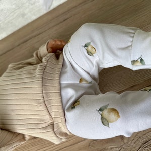 Puede incluir: Un beb&eacute; con una camisa de manga larga de color beige con textura de canal&eacute; y pantalones blancos con estampado de limones.