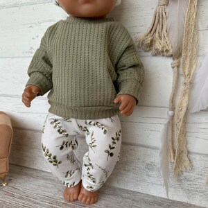 K&ouml;nnte beinhalten: Eine Puppe tr&auml;gt einen gr&uuml;nen Waffelstrickpullover und eine wei&szlig;e Hose mit gr&uuml;nem Blattmuster.