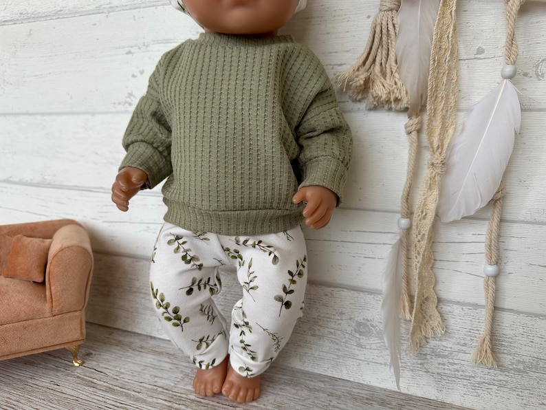 K&ouml;nnte beinhalten: Eine Puppe tr&auml;gt einen gr&uuml;nen Waffelstrickpullover und eine wei&szlig;e Hose mit gr&uuml;nem Blattmuster.
