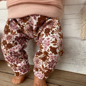 May include: A pair of brown and pink floral leggings for a baby or toddler. The leggings have a white background with brown and pink flowers.