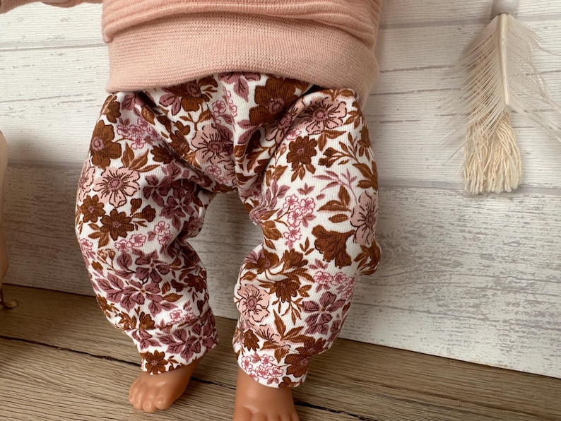 May include: A pair of brown and pink floral leggings for a baby or toddler. The leggings have a white background with brown and pink flowers.