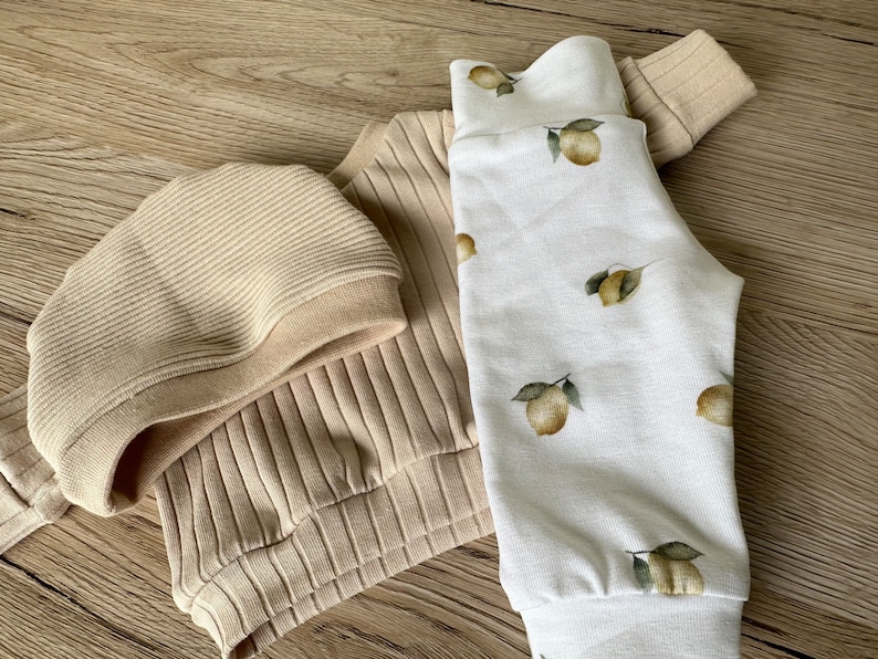 Puede incluir: Un su&eacute;ter beige de canal&eacute; y un gorro a juego con un pantal&oacute;n blanco con estampado de limones.