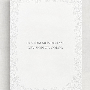 以下が含まれることがあります： 白い長方形のカードで、花のエンボス加工のボーダーが付いています。「CUSTOM MONOGRAM REVISION OR COLOR」というテキストが、濃いグレーのフォントでカードの中央に配置されています。カードはテクスチャ加工された表面です。