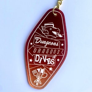 May include: A red and orange motel key chain with a white dragon and the text "Dungeons & Dragons Dives" with a fork, knife, and axe graphic.