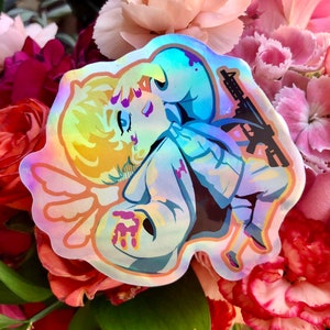 May include: A holographic sticker featuring a cartoon character with blonde hair and a white shirt, holding a gun and a bloody knife. The character has wings and is surrounded by a pink and blue halo.