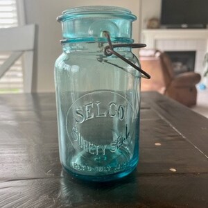 May include: A vintage blue glass jar with a wire bail closure. The jar has the text "SELCO SURETY SEAL PAT'D JULY 14, 1925" printed on the front.