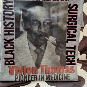 May include: A gray t-shirt with a black and white photo of a man wearing glasses and a suit. The text "BLACK HISTORY" is on the left side of the shirt, and the text "SURGICAL TECH" is on the right side of the shirt. The text "Vivien Thomas PIONEER IN MEDICINE" is at the bottom of the shirt.