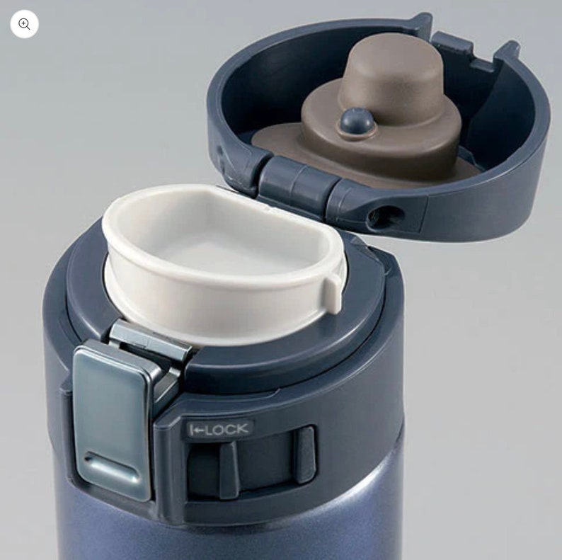 May include: A close-up of a blue insulated water bottle with an open lid. The lid is dark blue with a brown cap and a white drinking spout. A silver latch is visible, with the word "LOCK" printed on the side.