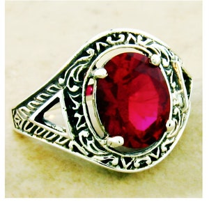 May include: A silver ring with an ornate design featuring a large, oval-shaped, red gemstone.