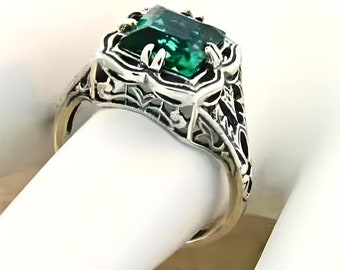 May include: A silver ring with an emerald green gemstone set in a filigree design.