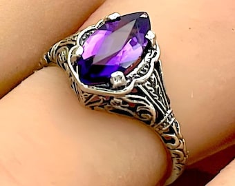 May include: A silver ring with an ornate design features a large, pear-shaped amethyst gemstone.