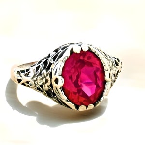 May include: A vintage ring with a large, bright red gemstone set in a filigree design.