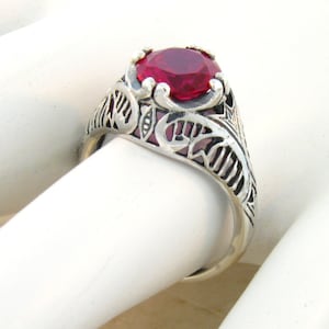 May include: A silver ring with an ornate design featuring a large, red gemstone.
