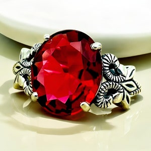 May include: A silver ring with a large, red, faceted gemstone surrounded by intricate floral designs.