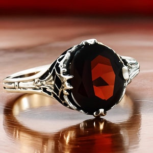 May include: A silver ring with a large, oval-shaped, dark red gemstone set in a detailed, ornate design.