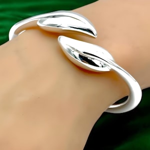 May include: A silver bangle bracelet with a leaf design. The bracelet is open and has a smooth, polished finish.