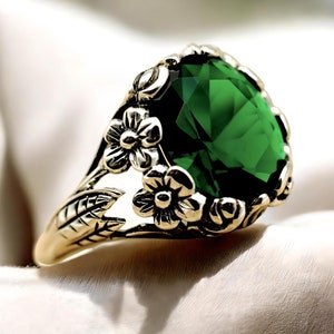 May include: A gold ring with a large, faceted, emerald green gemstone surrounded by floral details.