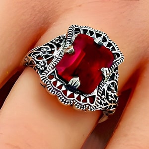 May include: A silver ring with a large, red, rectangular gemstone set in a filigree design.