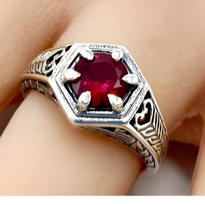 May include: A silver ring with an ornate design and a red gemstone in the center.