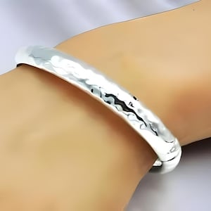 May include: A silver hammered bangle bracelet. The bracelet is smooth and shiny, with a hammered texture.