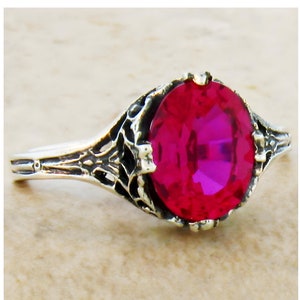 May include: A silver ring with a large, oval-shaped, bright pink gemstone set in a filigree design.