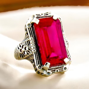 May include: A silver ring with an ornate design features a large, vibrant pink gemstone in a rectangular cut.