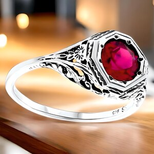 May include: A silver ring with a filigree design and a large, octagonal, red gemstone.