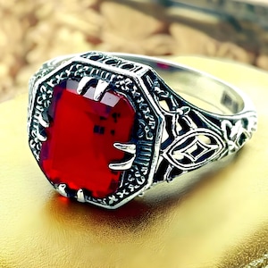 May include: A silver ring with an ornate design and a large, red gemstone.