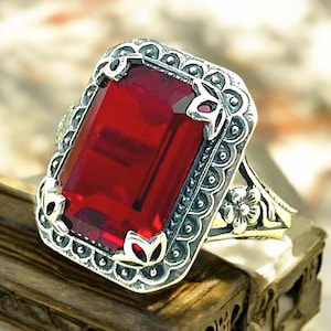 May include: A silver ring with a large, red, rectangular gemstone set in a floral design.