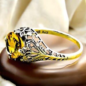 May include: A silver ring with a yellow gemstone set in a filigree design. The ring is marked "925" on the inside band.