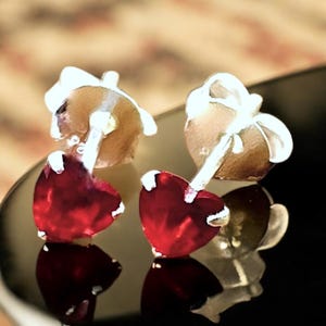 May include: A pair of silver heart-shaped stud earrings with red gemstone accents.